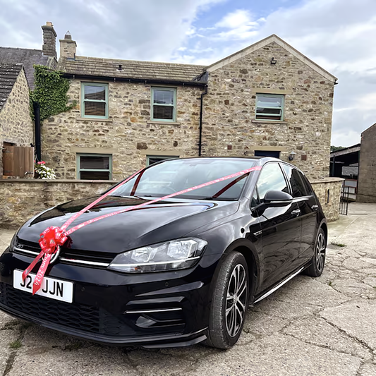 A red personalised wedding car ribbon kit on a black car.