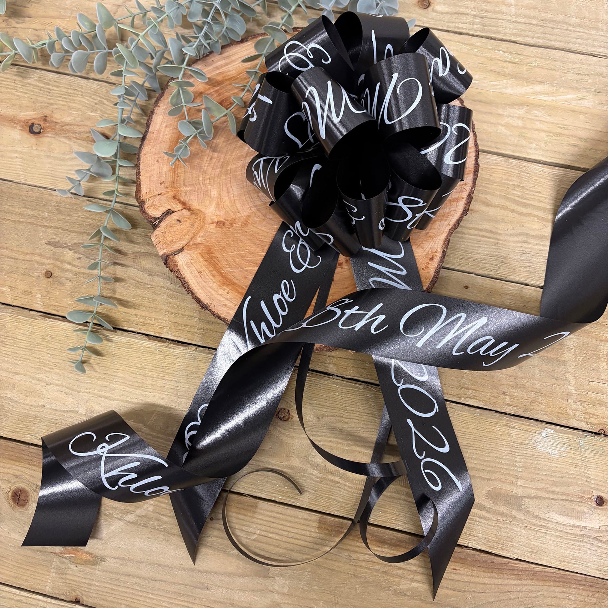 Black wedding car ribbon with white text on a wooden surface with greenery