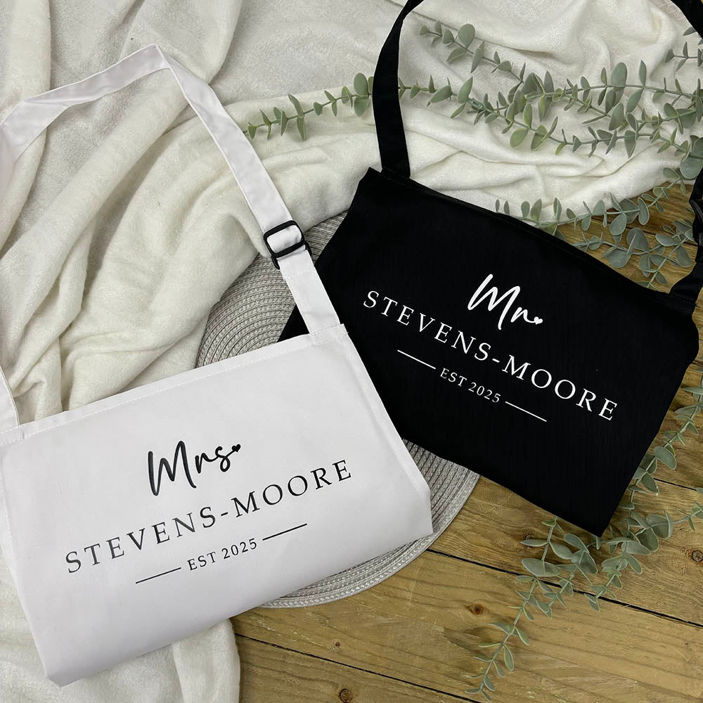 Two aprons, one white and one black, with 'Mrs. Stevens-Moore' and 'Mr. Stevens-Moore' text on a wooden surface.