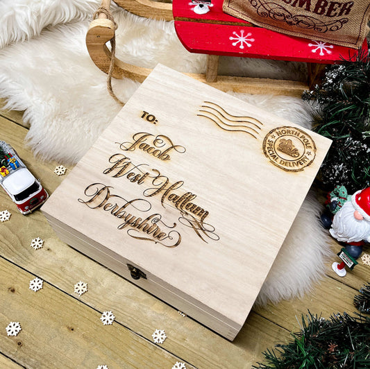A wooden Christmas Eve box with personalised engraving, closed and placed on a wooden surface with Christmas decorations around it.