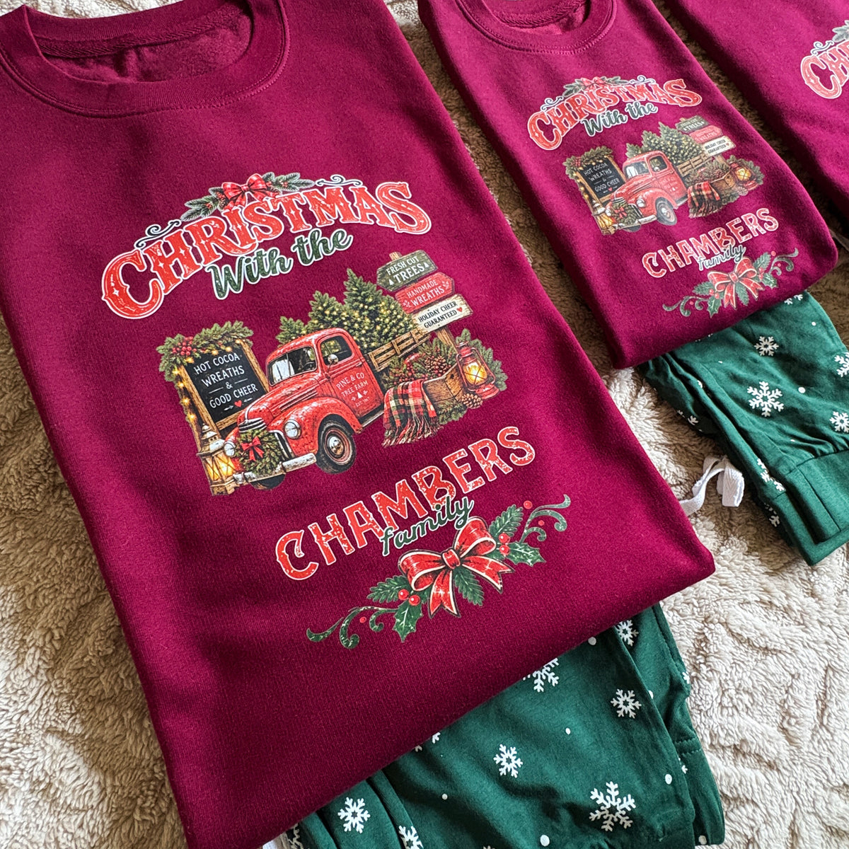 Christmas themed sweatshirt with a vintage red truck graphic and the words 'Christmas with the Chambers Family,' paired with green snowflake print pyjama bottoms on a beige textured blanket.