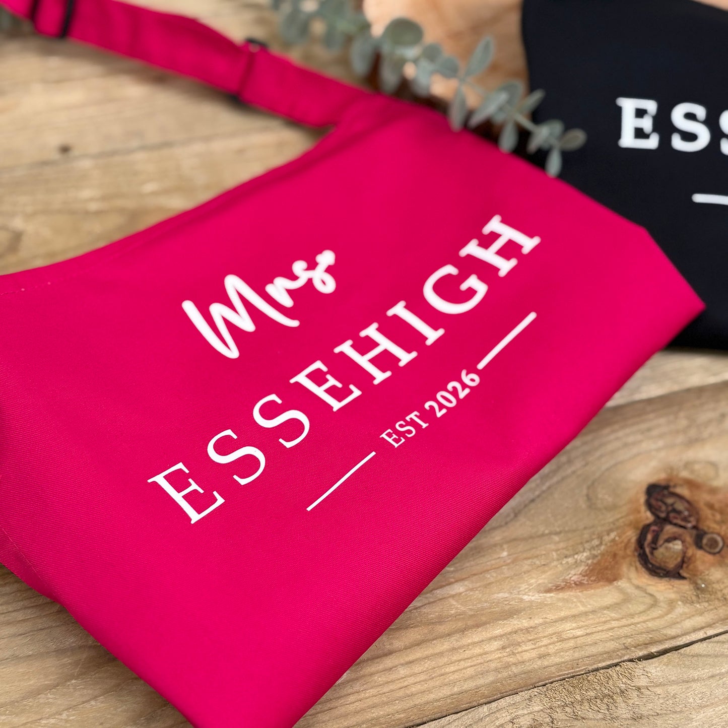 Pink apron with 'Mrs. ESSEHIGH EST 2026' text on a wooden surface