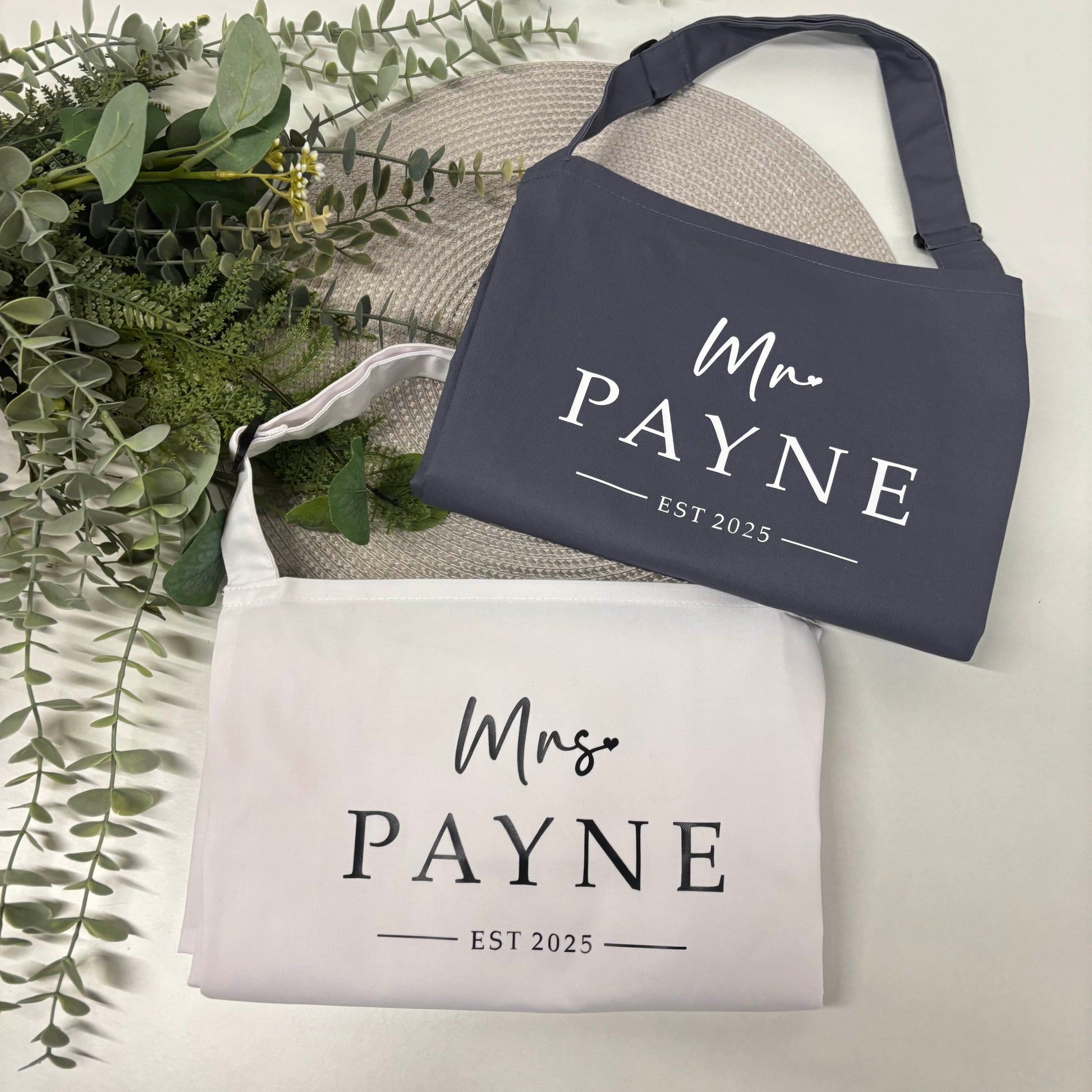 Couples Apron Set with 'Mr. Payne' and 'Mrs. Payne' text on a light background with greenery.
