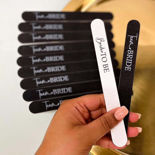 A hand holding a black team bride hen party nail file and a white bride to be nail file.