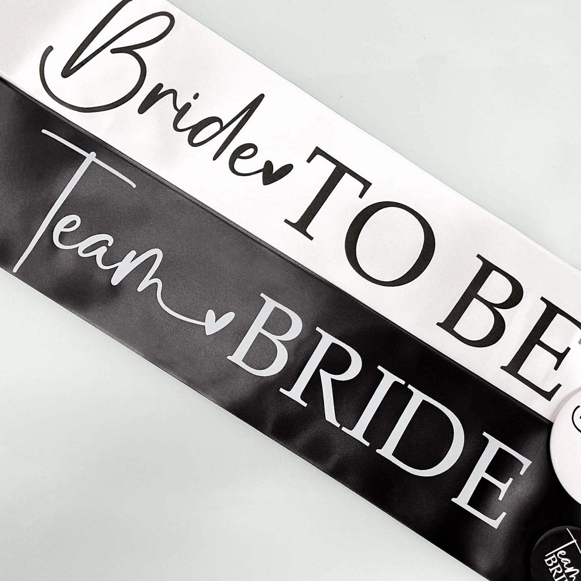 Black sash with 'Bride to Be' and 'Team Bride' text on a white background